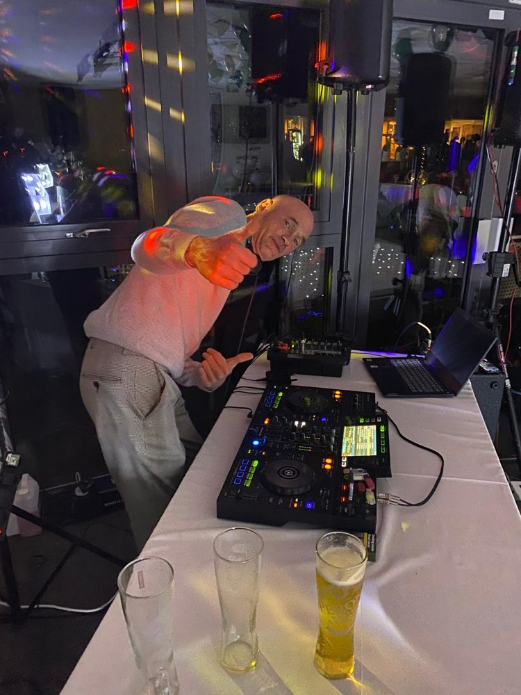 A DJ giving a thumbs up behind his decks at a party.