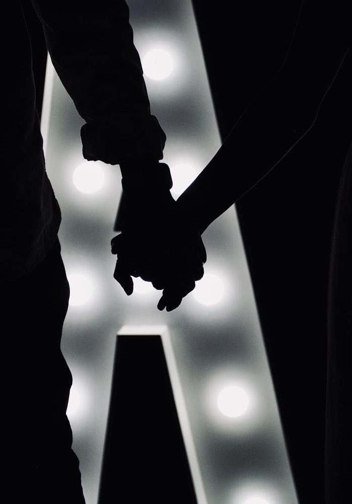 Two silhouetted people holding hands in front of a lit-up letter A.